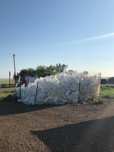 White pesticide containers are stacked inside of a wire fenced corral. 